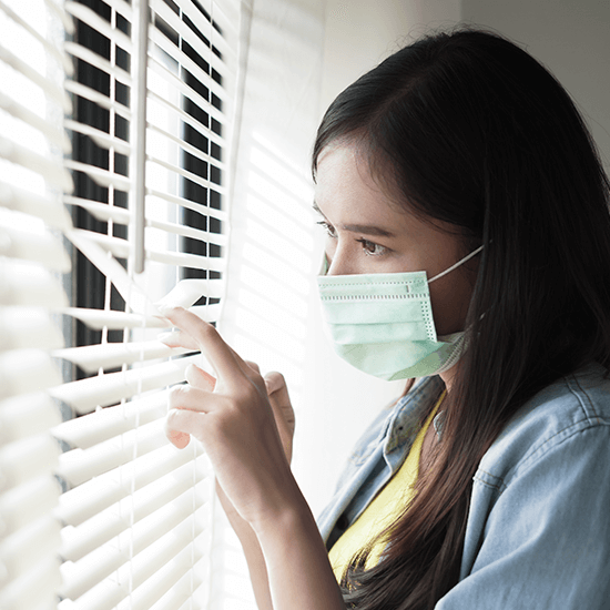 Young girl with depression wearing a mask and looking out of a window